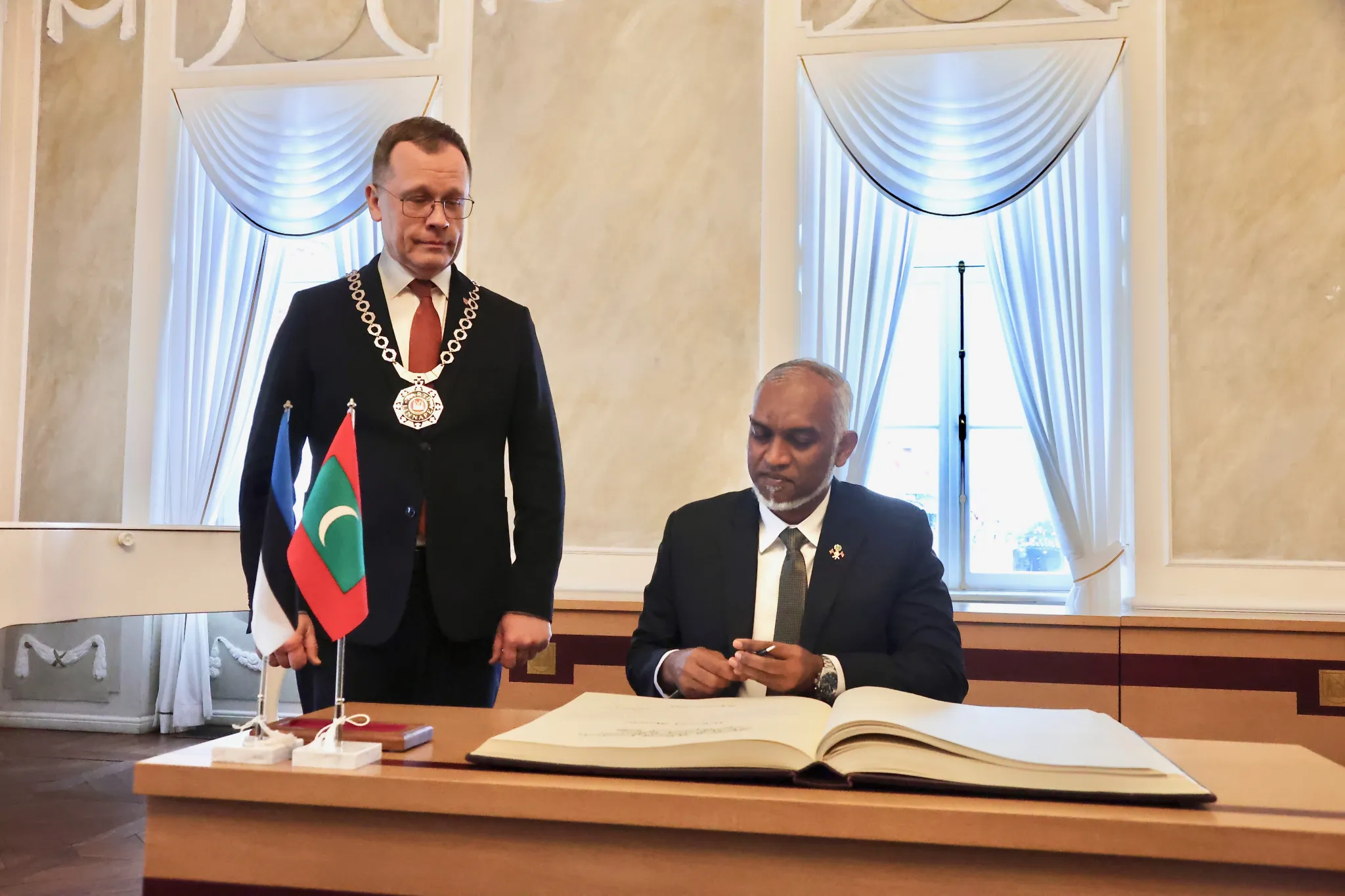 Pildil on Tartu linnapea Urmas Klaas tumedas ülikonnas, tema kõrval istub laua taga Maldiivi Vabariigi president Mohamed Muizzu. Laual on maldiivide ja eesti laualipud ning külalisteraamat.