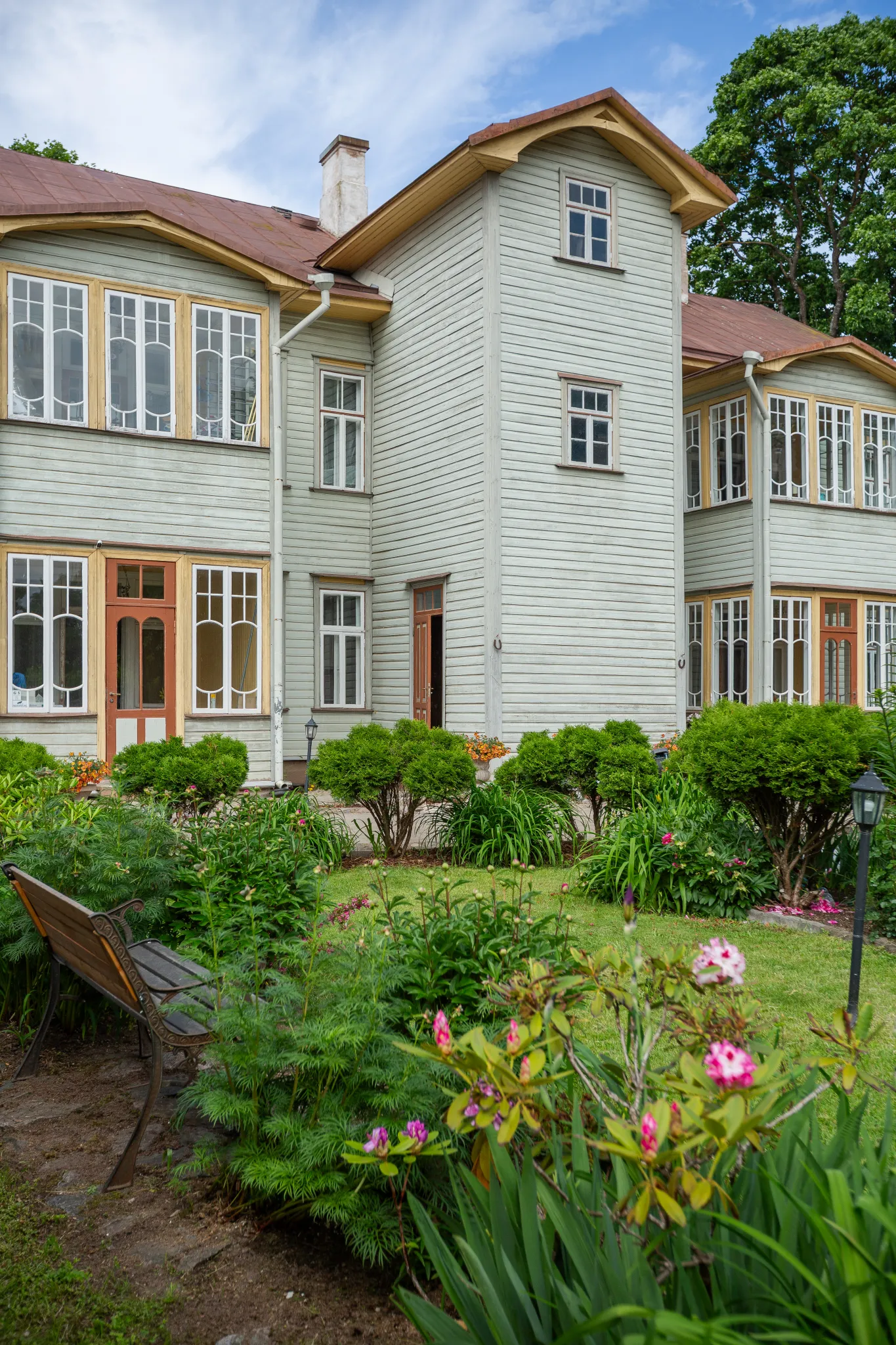  Tartu ajalooline puidust villamaja, keskse torniga ja suurte akendega, ümbritsetud lopsaka aiaga, roosade lilledega aed ning puidupink.