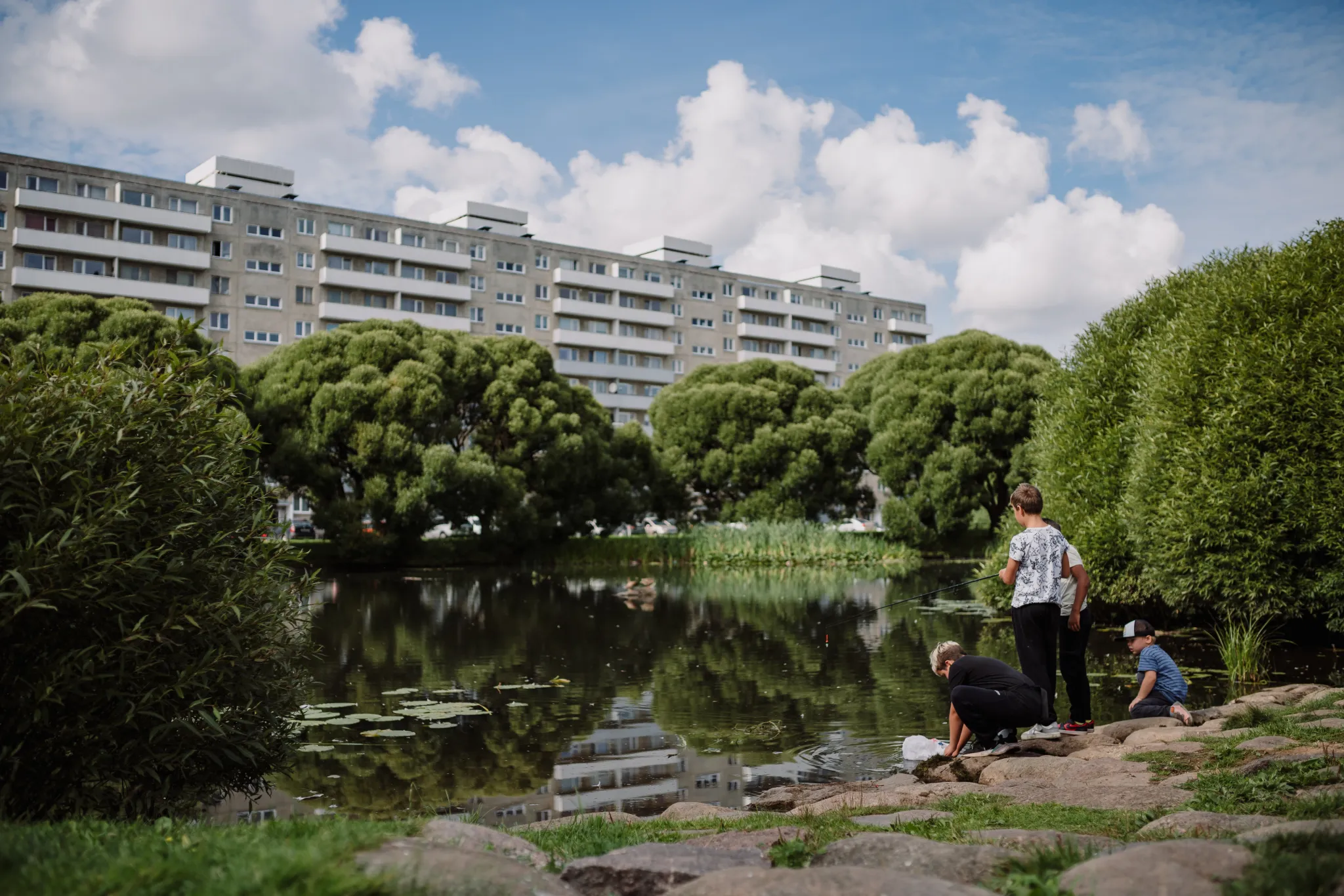Poisid tiigi ääres kalastamas, taustal üheksakorruseline Annelinna kortermaja