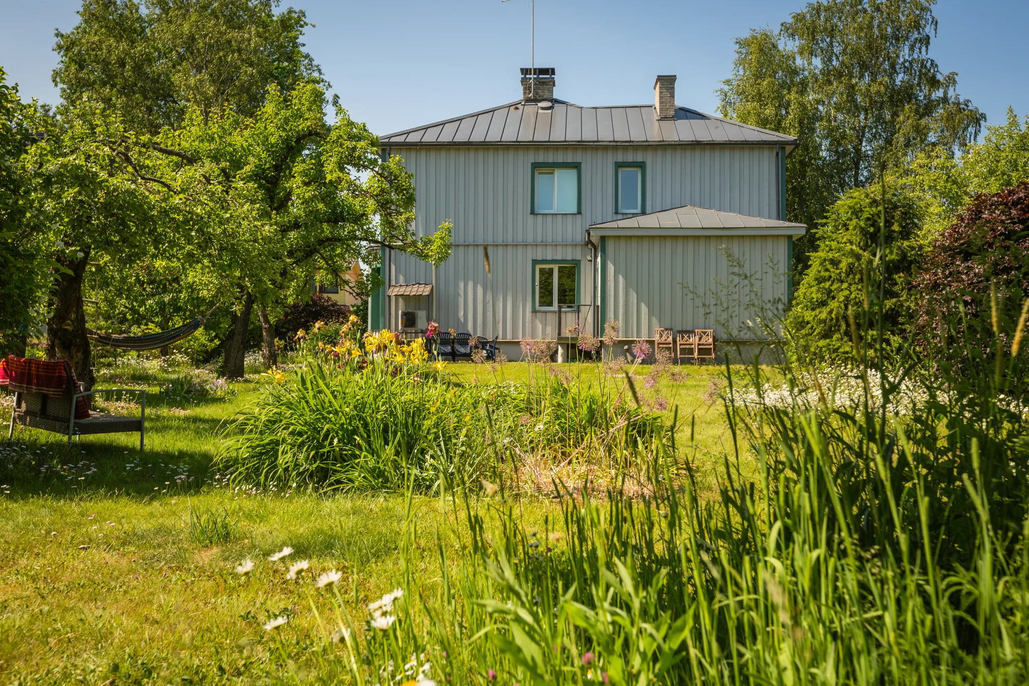  Lopsakas roheline aed, valge aiarkatus, värvikad taimed, väikene roosiline maja ning puidust aianõud.