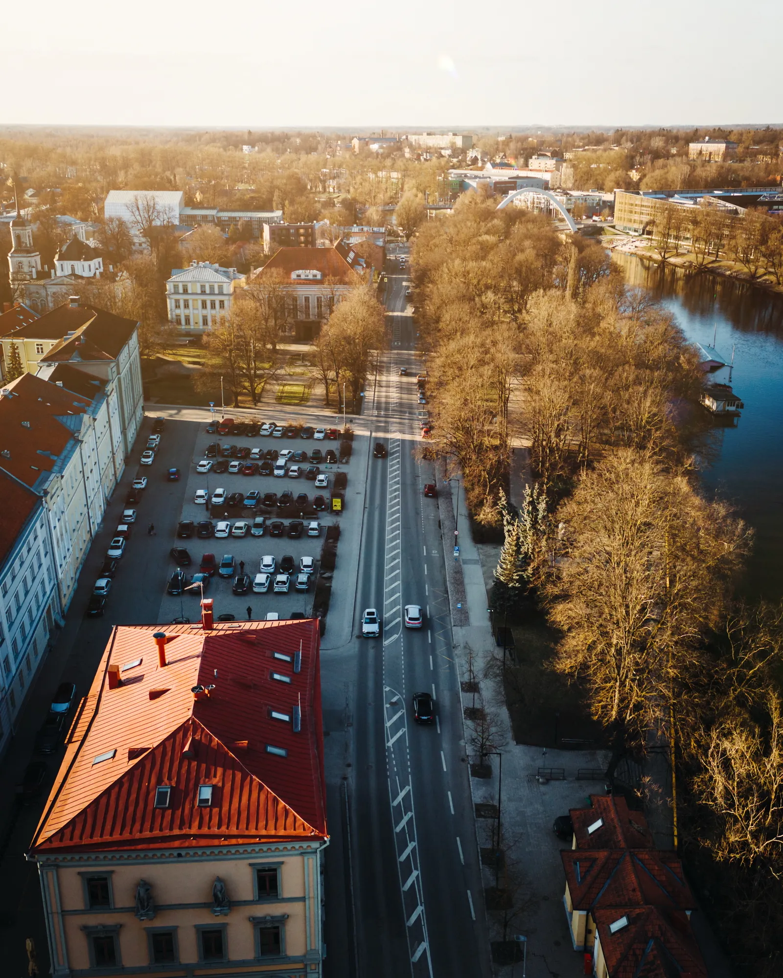  Õhust vaade Tartu keskustele, näha tänav, parkla, ajaloolised hooned, puud ja Emajõgi jõe taustal selges taevas.