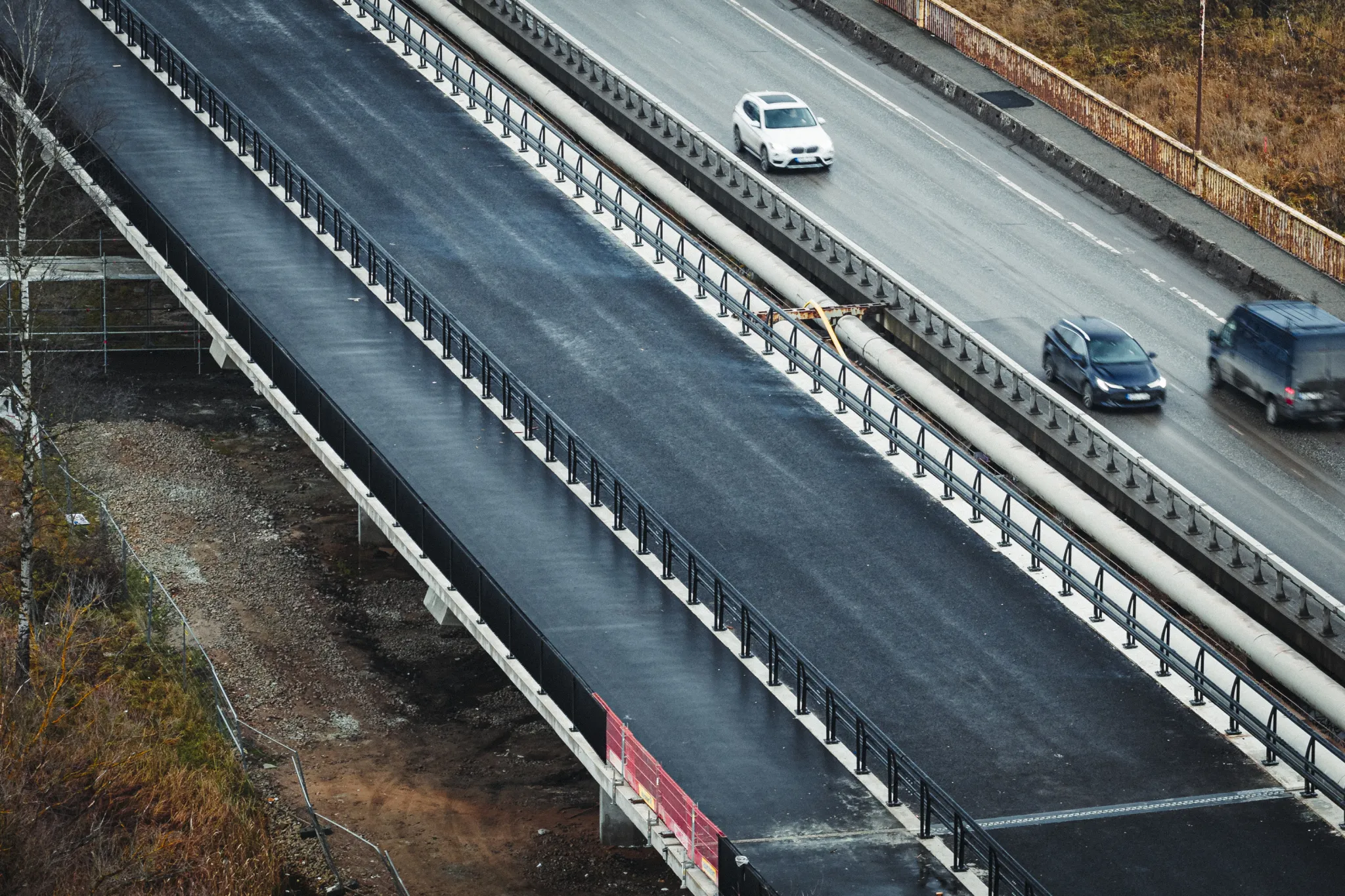  Õhust vaade mitme-liinilisele kõrgendatud maanteele ja piiretega. Sõidukid liiguvad ülemisel teel, kõrval on paralleelne tee; servades on sügisesed puud.
