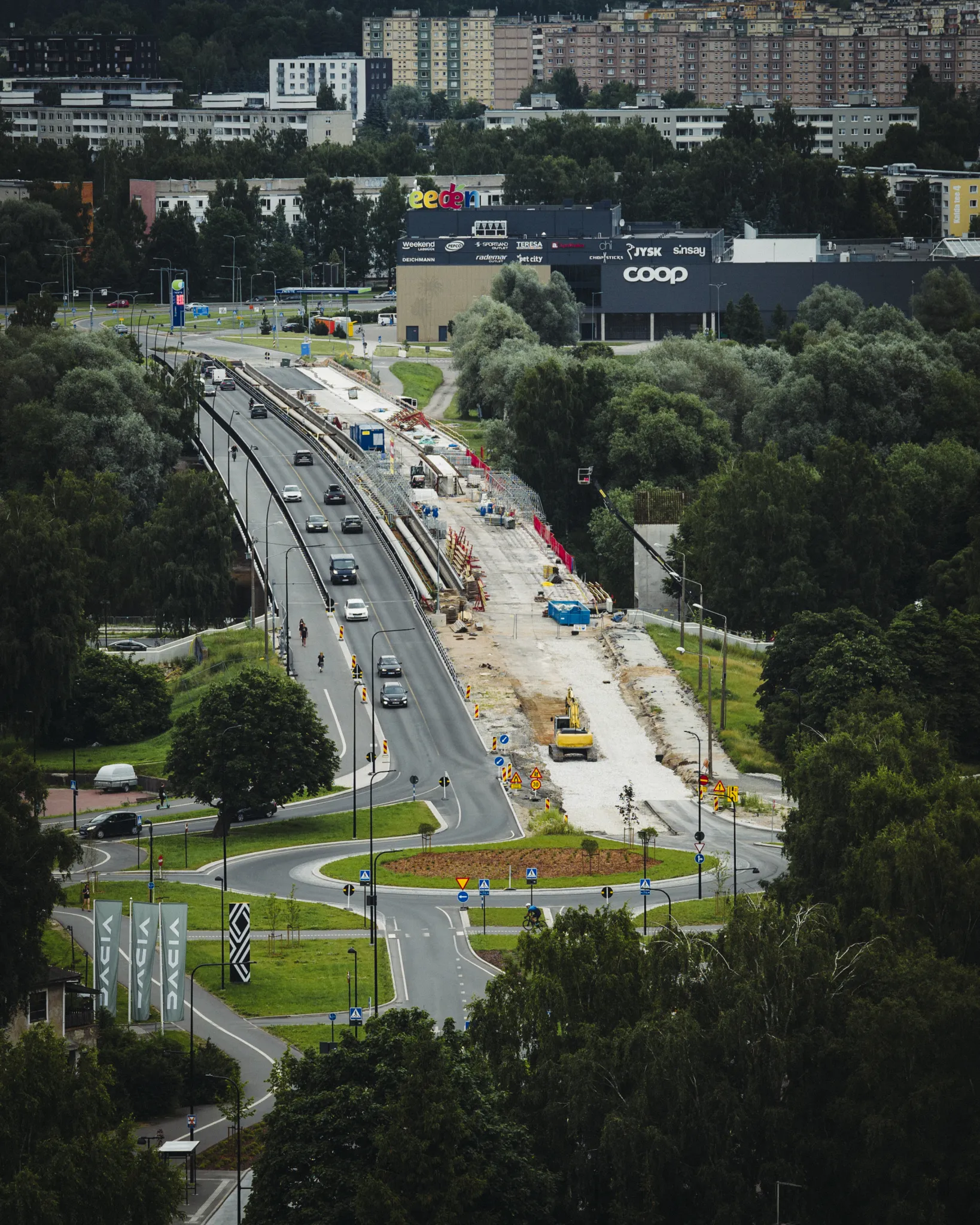  Tartu linnapilt: suure tee ääres teehooldustööd, ringtee ja liiklus; puud raamivad ala, taustal Coopiga jaemüügikeskus.