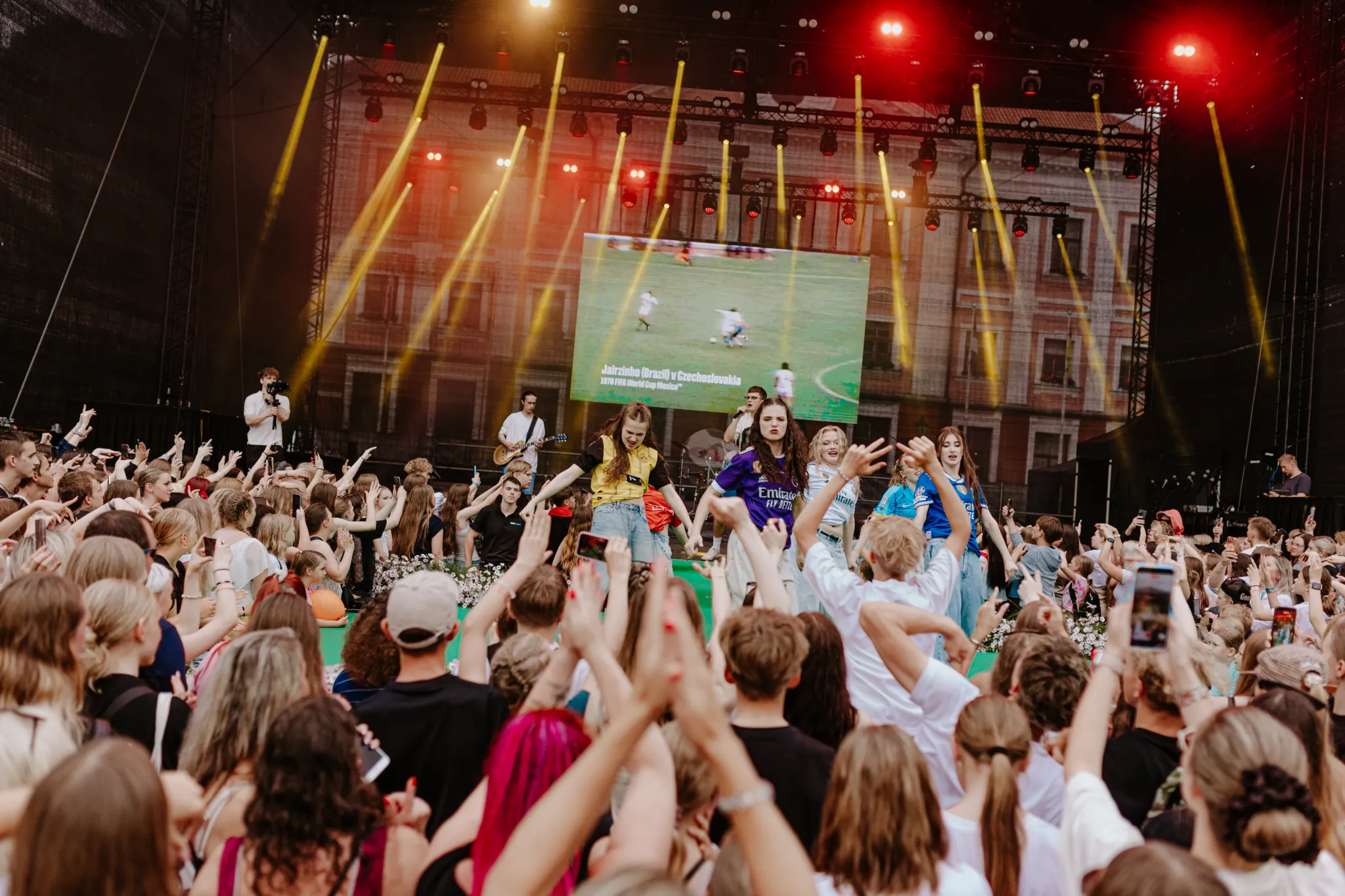  Vabaõhukontsert täis rahvast, käed õhku tõstetud, laval esinejad ja eredad valgusvihud. Suur ekraan taustal ning värvikirevad valgusvihud loovad öises linnamelus festivaliõhtu vibe.