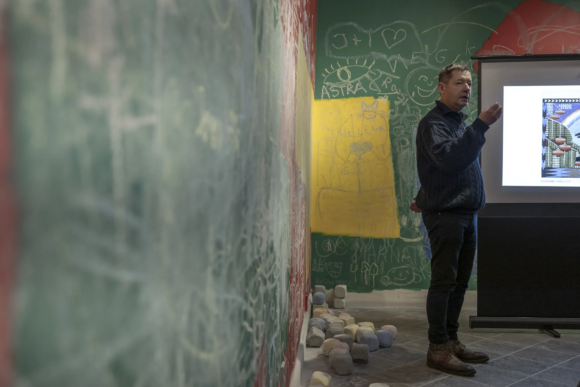 ** Esineja tutvustab teavet ekraani ees loovalt kaunistatud ruumis, kus on kriidivärvi seinad. Esitlus toob esile värvikad illustratsioonid, luues kaasahaarava õpikeskkonna.