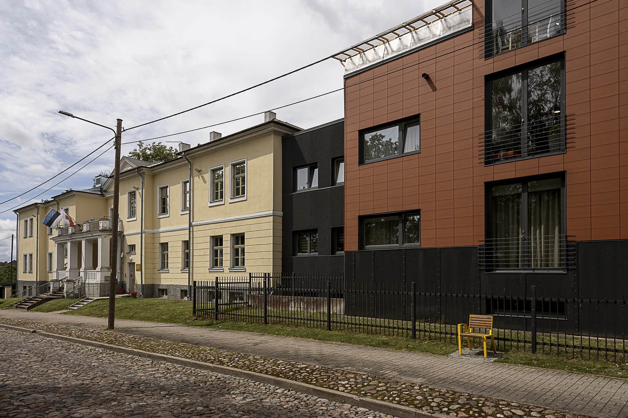 Liiva tänava vaade, kus on näha ajaloolise ja modernse arhitektuuri segu. Hooned eristuvad erksate värvide ja erinevate stiilidega, rõhutades linna traditsiooni ja innovatsiooni segu. Kiviplaatidega tänav lisab võlu.