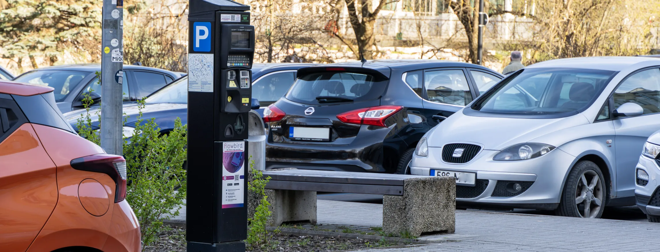  Tartu, Eesti tänavapilt: pargimasin, pink ja rivis pargitud autod; taustal paljad puud.