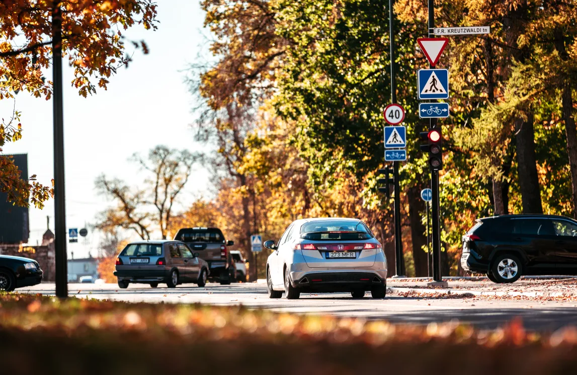 Autod sõidavad sügisesel Tartu tänaval kuldsete puude ja liiklusmärkide all.