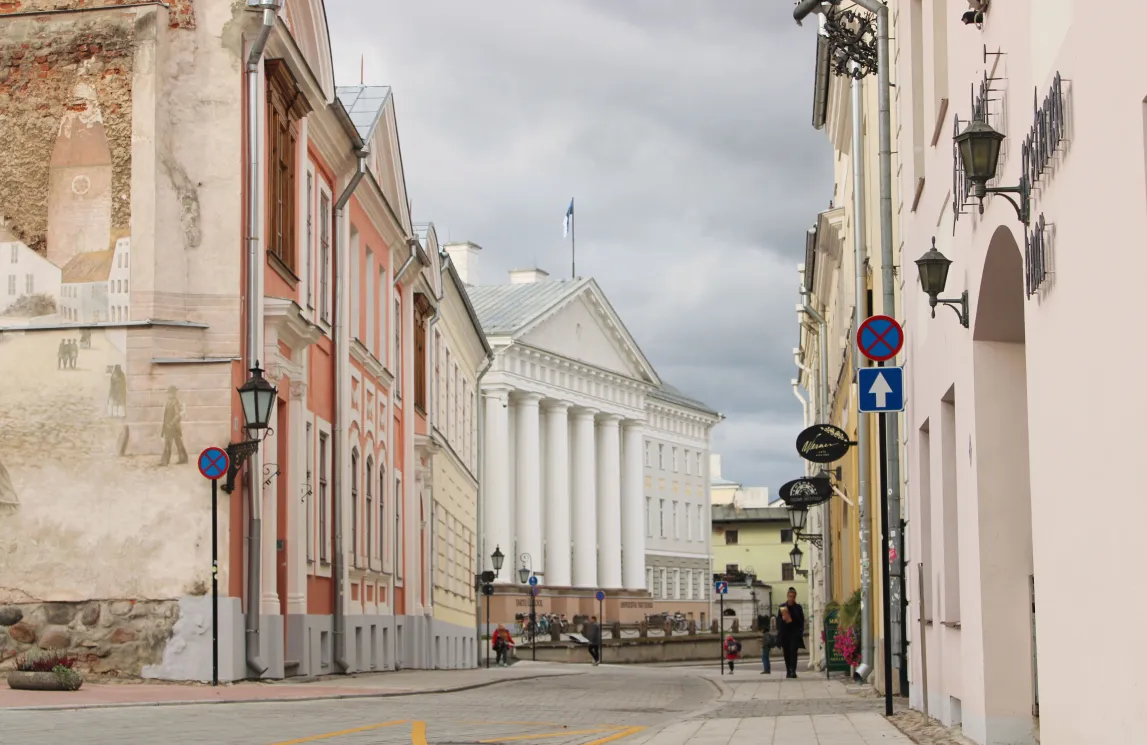 Tänavavaade Tartu kesklinnas. Keskel on näha Tartu Ülikooli peamaja valgete sammastega fassaad, mõlemal pool tänavat ajaloolised hooned.